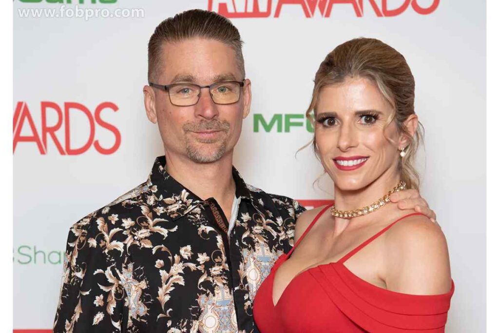 "Cory Chase Net Worth—couple at awards event with husband in floral shirt and woman in red dress"